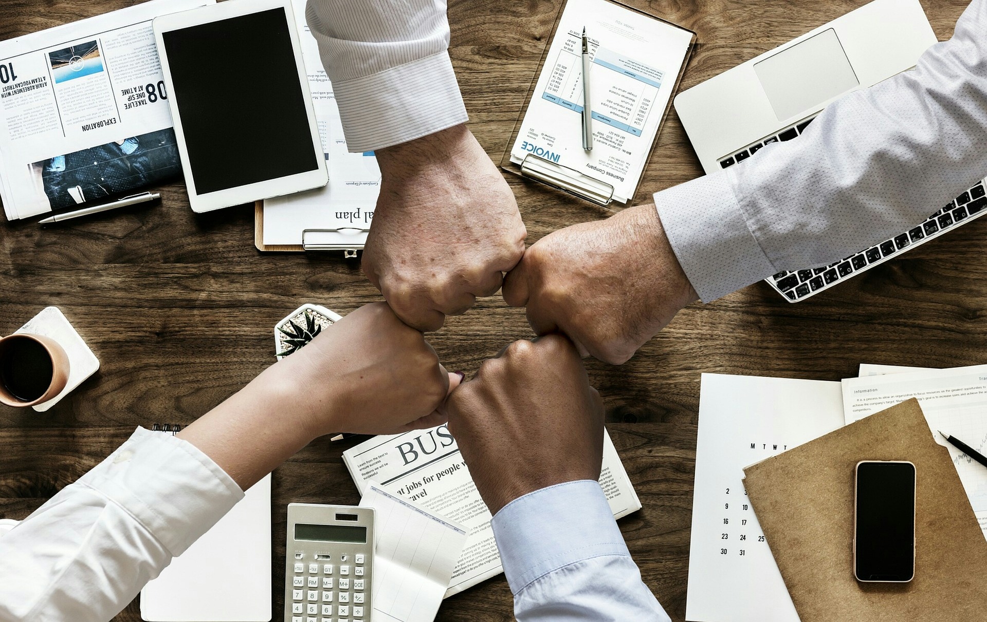 pozytywny employer branding stykające się dłonie czterech osób nad stołem w biurze, jako symbol poparcia i współpracy