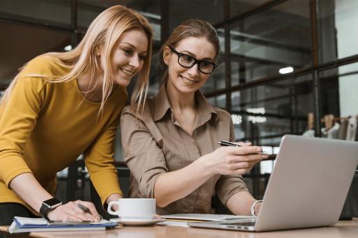 dwie kobiety w pracy przy biurku szukają czegoś na laptopie